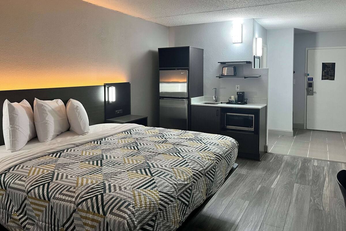 A hotel room with a large bed, a kitchenette, a small desk, and a bathroom.
