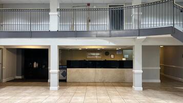 A spacious lobby with a reception desk, a second-floor balcony, and a tiled floor.