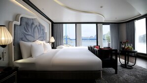 A modern hotel room with a large bed, a view of the sea, and a small table with a bottle and glasses. - Lotus D'Orient Cruise (Tuan Chau)