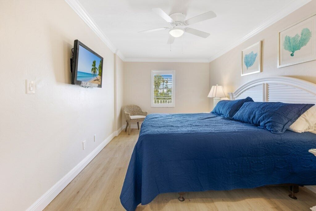 Un dormitorio con cama, ventilador de techo, televisión montada en la pared y ventana con persianas.