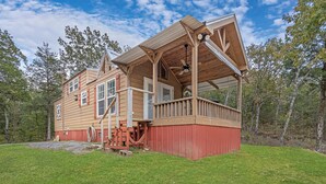 A two-story wooden house with a porch, a fenced yard, and a clear sky. - Cozy Tiny Cabin with a View!! (Decatur)