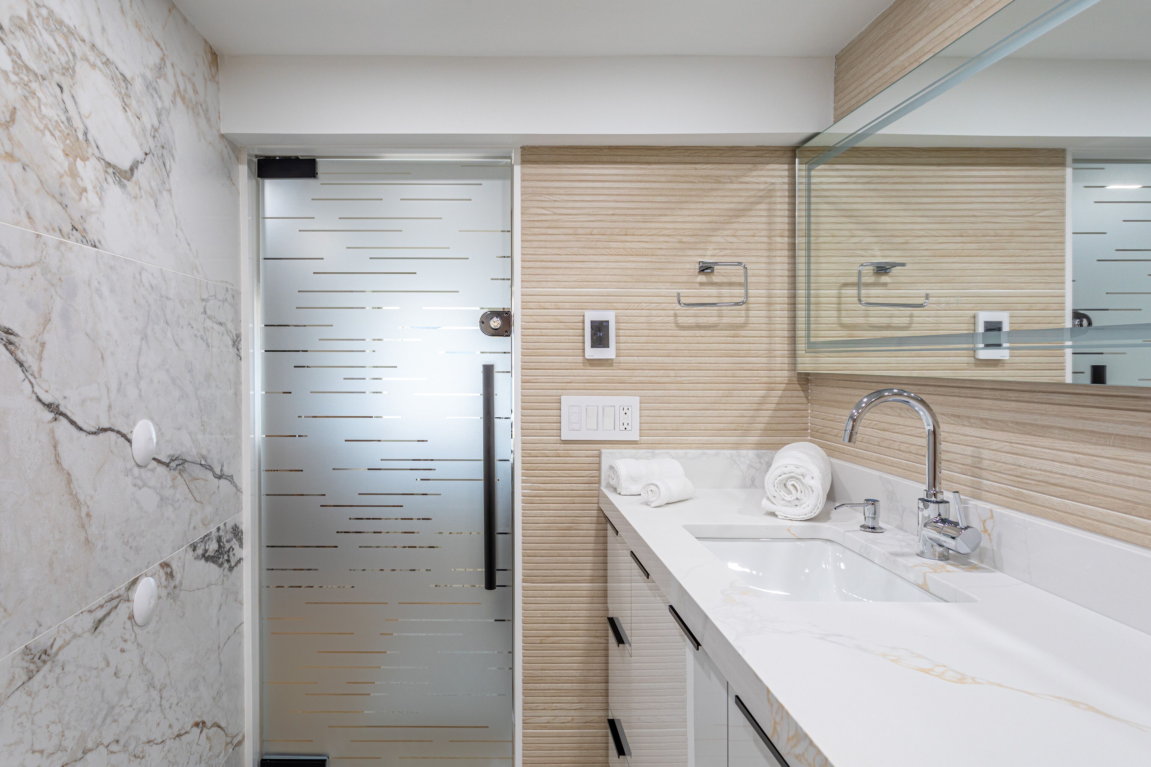 Une salle de bain moderne avec un mur en marbre, un mur recouvert de panneaux en bois, un lavabo avec un miroir et un porte-serviettes.