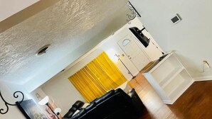 Un salon avec un canapé noir, un rideau jaune et une porte blanche.