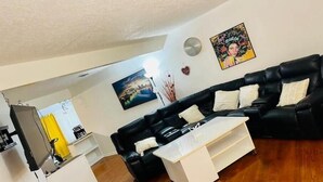 Un salon avec un canapé en cuir noir, une table basse blanche et un tableau accroché au mur.