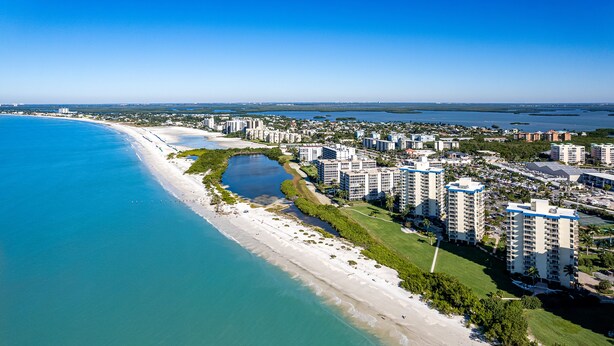 An aerial view of a coastal residential area with beachfront properties, a marina, and a clear blue sky. - Estero Beach and Tennis (Fort Myers Beach)