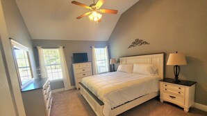 Une chambre à coucher comprenant un lit, des tables de chevet, une commode, un ventilateur de plafond et des fenêtres.