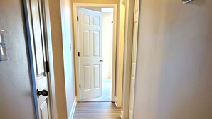 Un couloir au plancher de bois et aux moulures blanches, qui mène à une porte au fond.