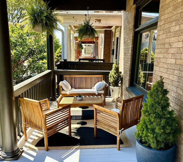 A wooden outdoor seating area with a bench and chairs, a small table, and a potted plant.