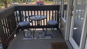 A balcony with two chairs and a small table, overlooking a parking area with cars and trees.