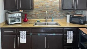 A kitchen with dark cabinets, a built-in oven, a microwave, a sink, and a stone backsplash.