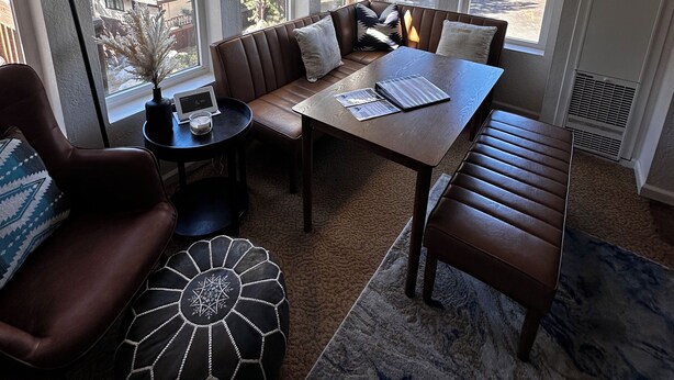 A cozy living room with a brown leather sofa, a wooden coffee table, and a patterned ottoman.