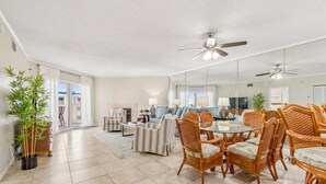 A spacious living room with a dining area, large windows, and a ceiling fan. - Beach Cottages Ocean & Pool View Condo (Indian Shores)