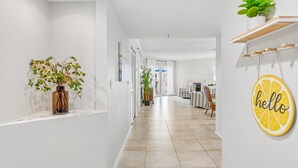 A hallway with a plant, a 'hello' sign, and a dining area in the distance. - Beach Cottages Ocean & Pool View Condo (Indian Shores)