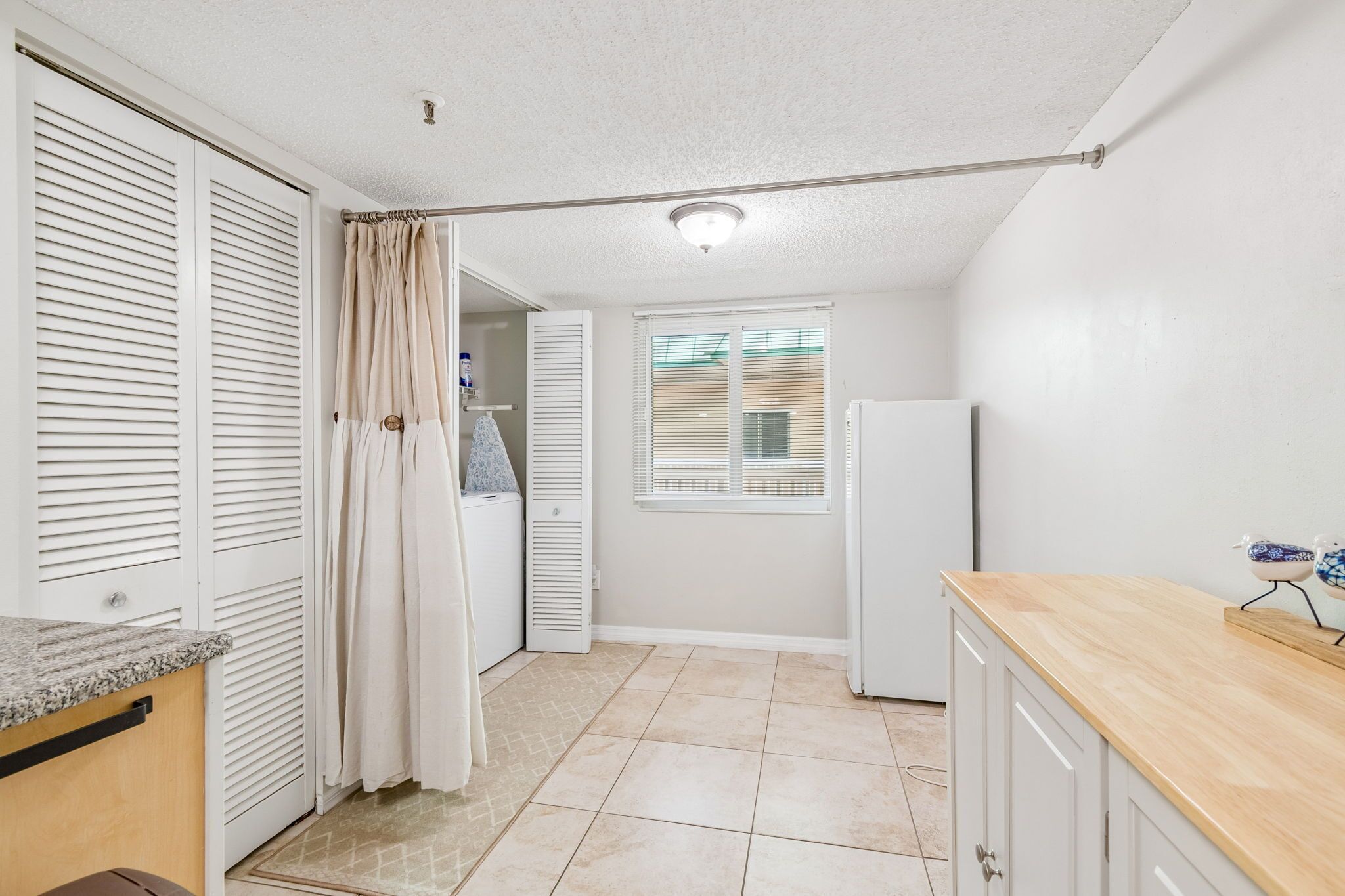 A compact kitchen with a countertop, a refrigerator, and a window with blinds.