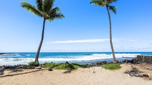 Uma praia com duas palmeiras, ondas do oceano e um céu azul límpido.