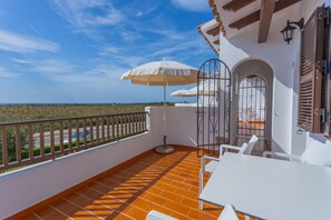 Enjoy the sea view from this balcony with a tiled floor, table, chairs, and umbrellas providing shade.