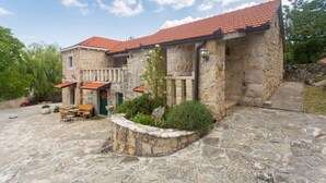 A stone building with a red-tiled roof, a stone patio with outdoor furniture, and a garden area. - Villa Brkic with private pool and playground- ideal for families & friends (Dicmo Osoje)
