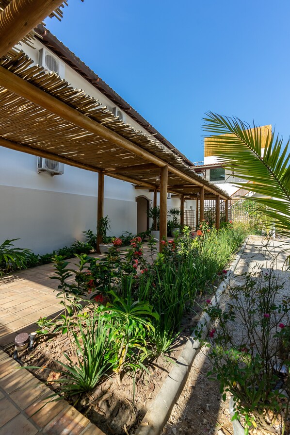 A covered outdoor area with a pergola, potted plants, and a pathway leading to a building. - Villa Alexandre Pousada (Porto Seguro)