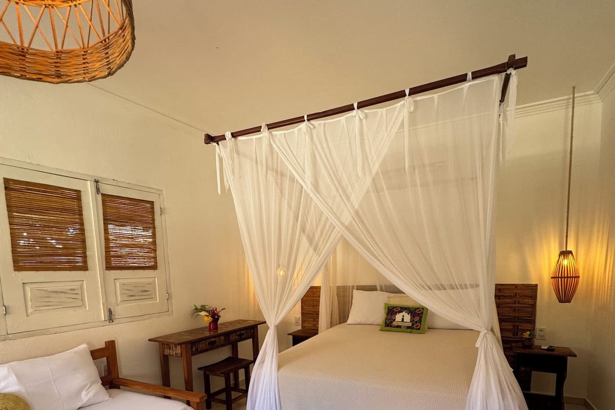 A bedroom with a four-poster bed, a bedside table, a nightstand, and a small desk with a chair.