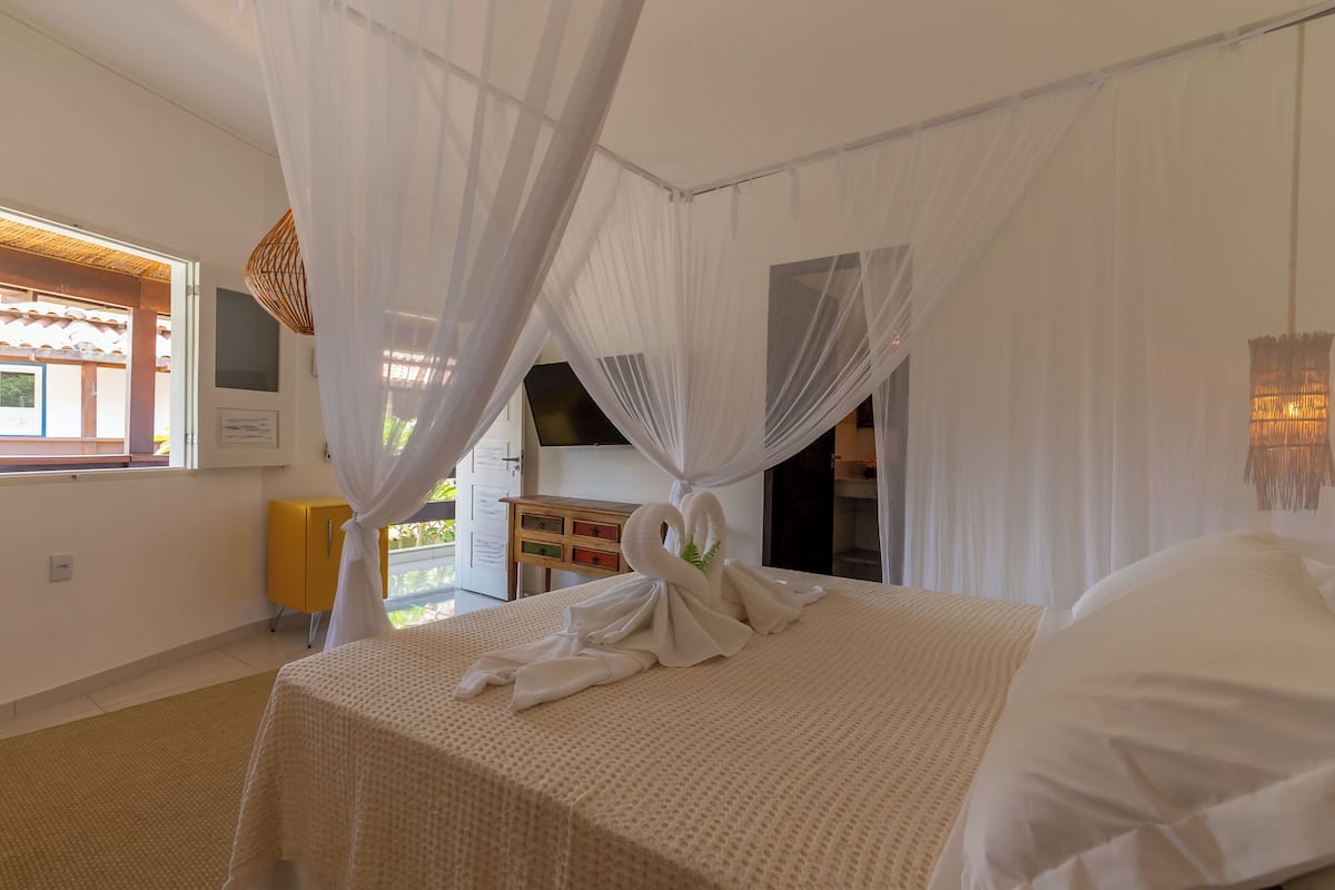 A bedroom with a bed, white curtains, a yellow cabinet, and a window.