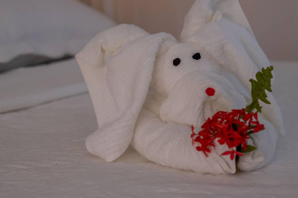 A towel animal with red flowers on a bed.