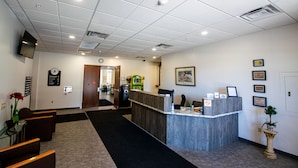 A reception area with a counter, seating, a clock, and a door leading to another room. - Rochester Hotel (Rochester)