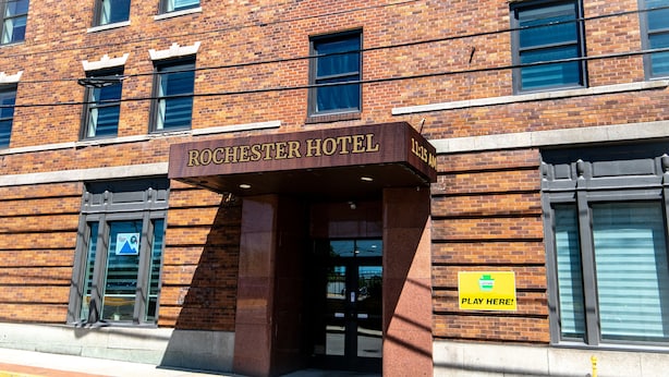 The Rochester Hotel entrance with a brick facade, large windows, and a sign indicating a Play Here! area. - Rochester Hotel (Rochester)