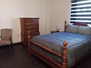 Une chambre à coucher avec un lit en bois, une commode, une chaise et une table de chevet.