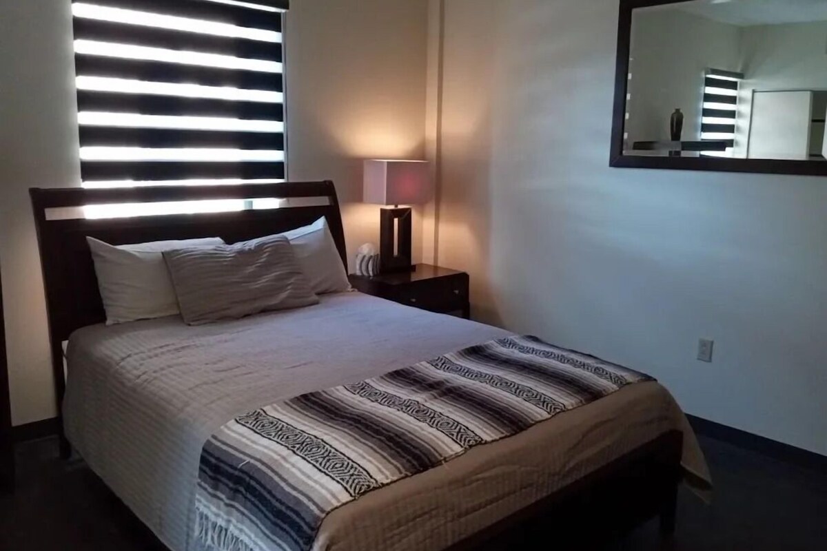 Une chambre à coucher avec un lit, une lampe de chevet, un miroir et une fenêtre avec des stores.