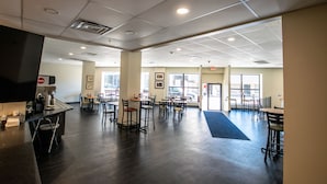 A spacious indoor area with multiple tables and chairs, a coffee machine, and large windows allowing natural light. - Rochester Hotel (Rochester)