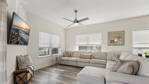 A modern living room with a sectional sofa, a ceiling fan, and large windows with blinds.