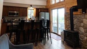 Ein geräumiges Wohnzimmer mit hoher Decke, Holzbalken, einem Kamin aus Stein und einer Küche mit modernen Geräten.