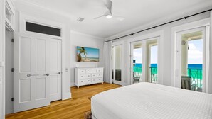 A bedroom with a large bed, white walls, wooden flooring, a ceiling fan, and a painting of a beach scene. - BellaVista on the Beach*HotTub*Gulf Front*3 Patios (Miramar Beach)