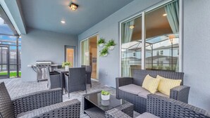 Eine Terrasse im Freien mit Korbmöbeln, einem Grill und großen Fenstern.
