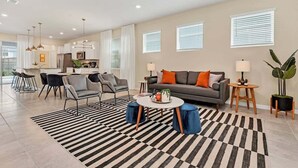 Ein modernes Wohnzimmer mit Sofa, Sesseln, einem Couchtisch und einer Küche im Hintergrund.