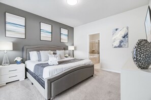 A bedroom with a bed, bedside tables, a nightstand, a bathroom with a shower, and artwork on the walls.