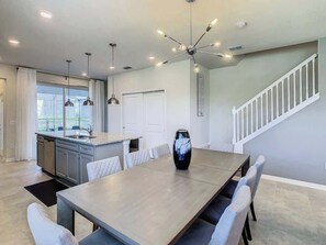A modern kitchen with a dining area, a staircase, and pendant lighting.