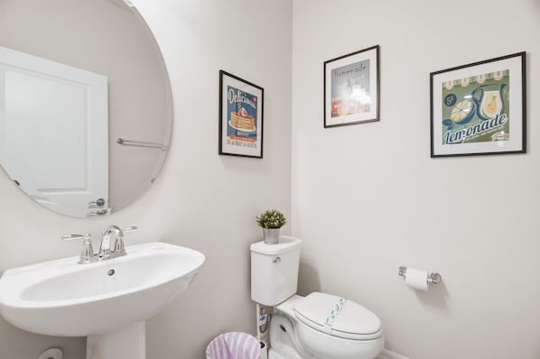 A bathroom with a white sink, a toilet, and two framed pictures on the wall.