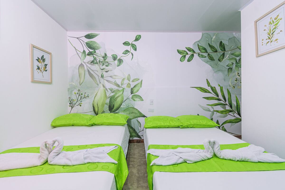 A hotel room with two beds, each with green bedding and white towels.