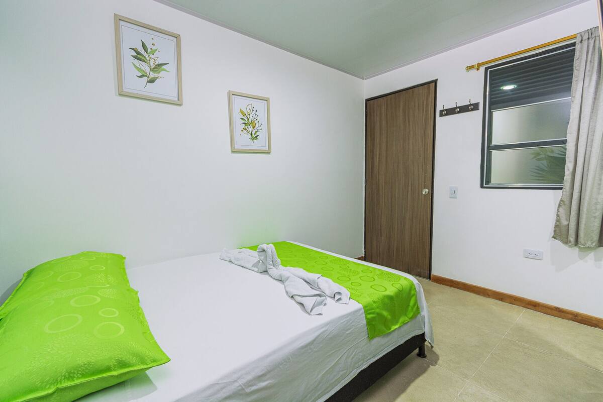 A bedroom with a bed, a window, and two framed botanical prints on the wall.