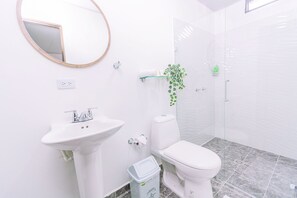 A bathroom with a pedestal sink, toilet, and a glass shower enclosure. - Nómada Hotel Guatapé (Guatapé)