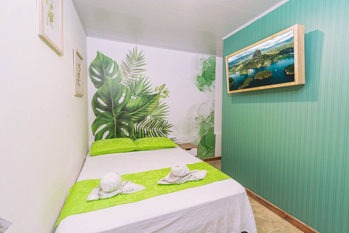 A hotel room with a bed, a green wall, and a framed picture of a landscape.