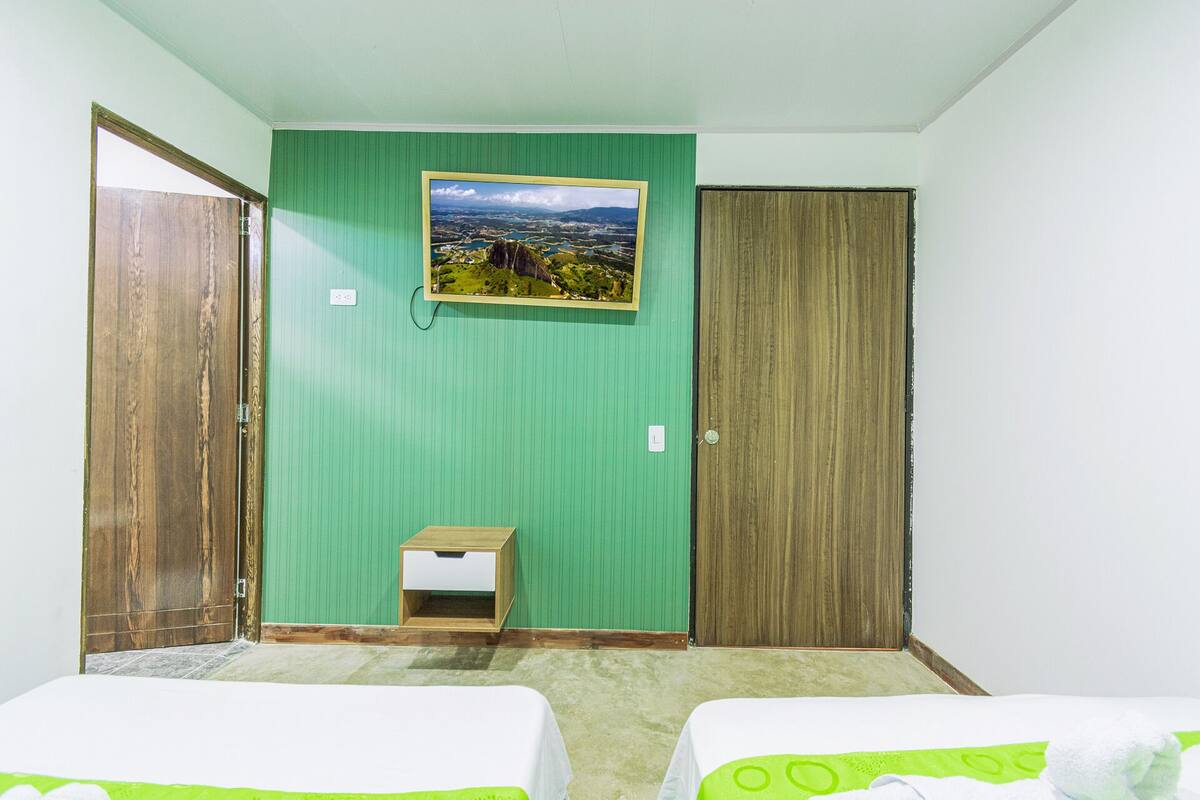 A room with two beds, a wooden door, a green wall, and a framed picture.