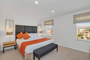 Une chambre à coucher avec un lit, des tables de chevet, un banc et des fenêtres équipées de stores.