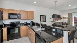 A modern kitchen with a microwave, stove, and dishwasher, a dining area with a table and chairs, and a living room with a sofa and a lamp.