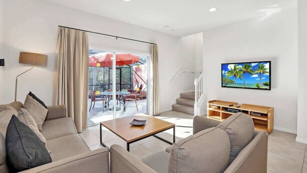 A modern living room with a sofa, coffee table, TV, and a sliding glass door leading to an outdoor area.