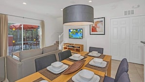 A dining area with a table set for four, a sofa, and a television on the wall.
