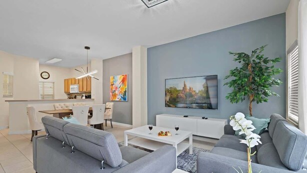 Een moderne woonkamer met een grijze bank, een witte salontafel en een aan de muur bevestigde televisie.