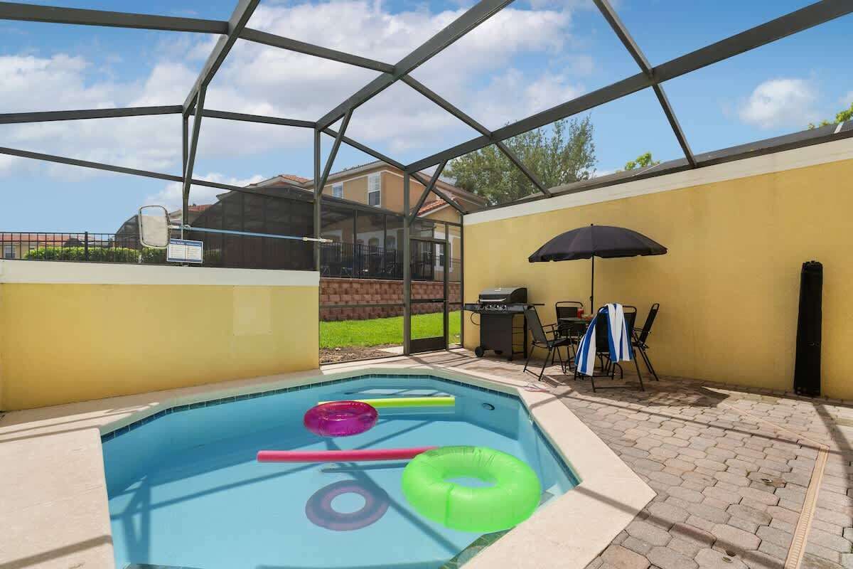 A covered swimming pool with inflatable rings, a grill, and patio furniture.