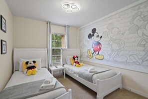 Een slaapkamer met twee bedden, een muurschildering van Mickey Mouse en een raam met jaloezieën.